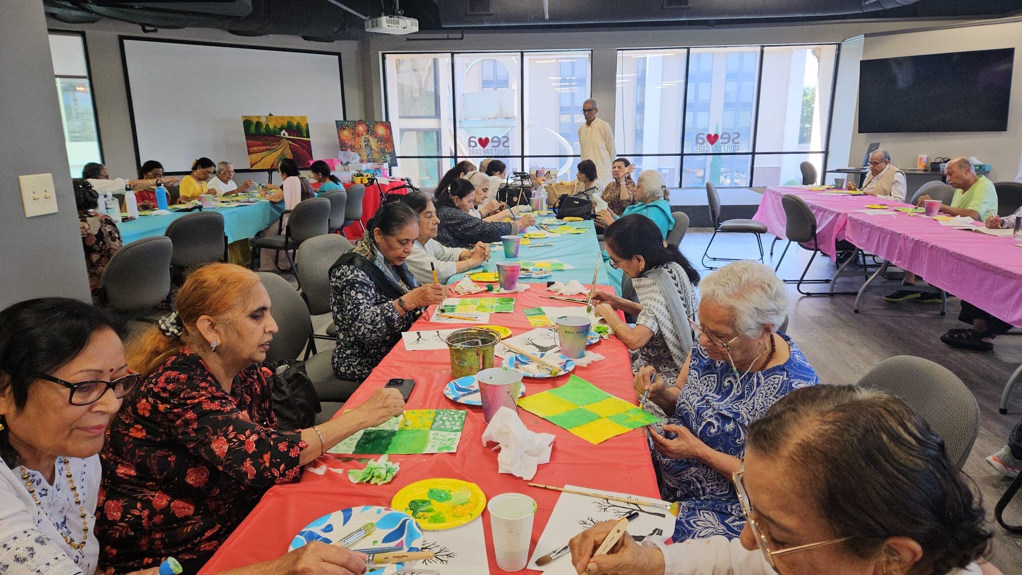 Members painting together at long tables during an art class