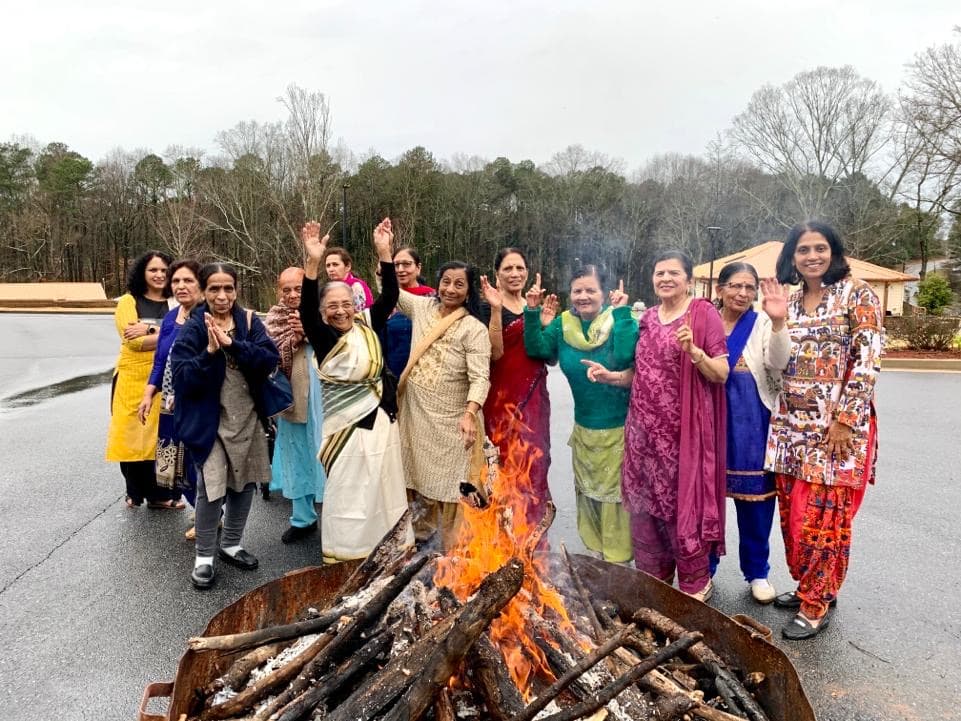 Members gathered around a bonfire for a Lohri celebration, hands raised