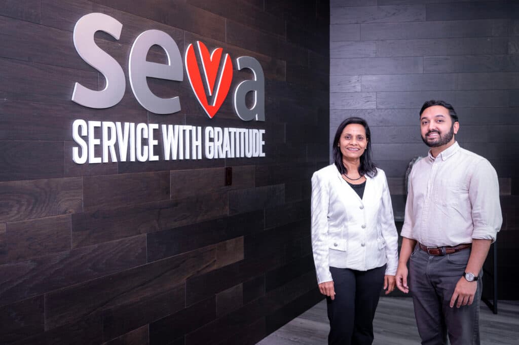 Poonam Datta and Chirag Datta standing beside the Seva Service with Gratitude sign