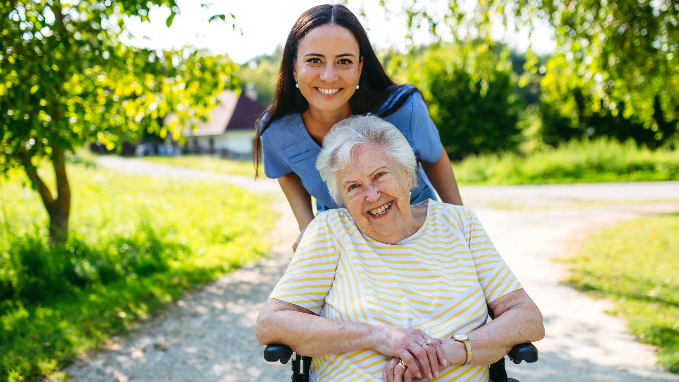 A caregiver and a smiling senior woman outdoors on a garden path
