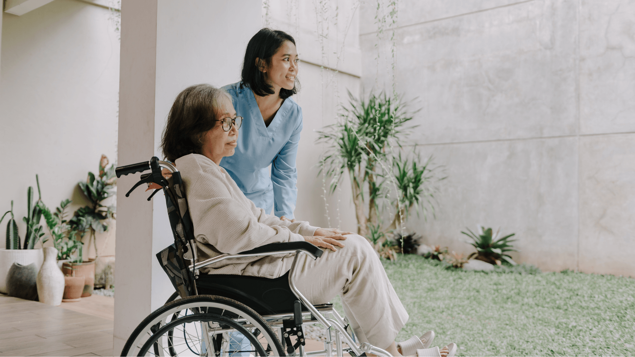 A caregiver with a senior woman in a wheelchair beside a bright garden