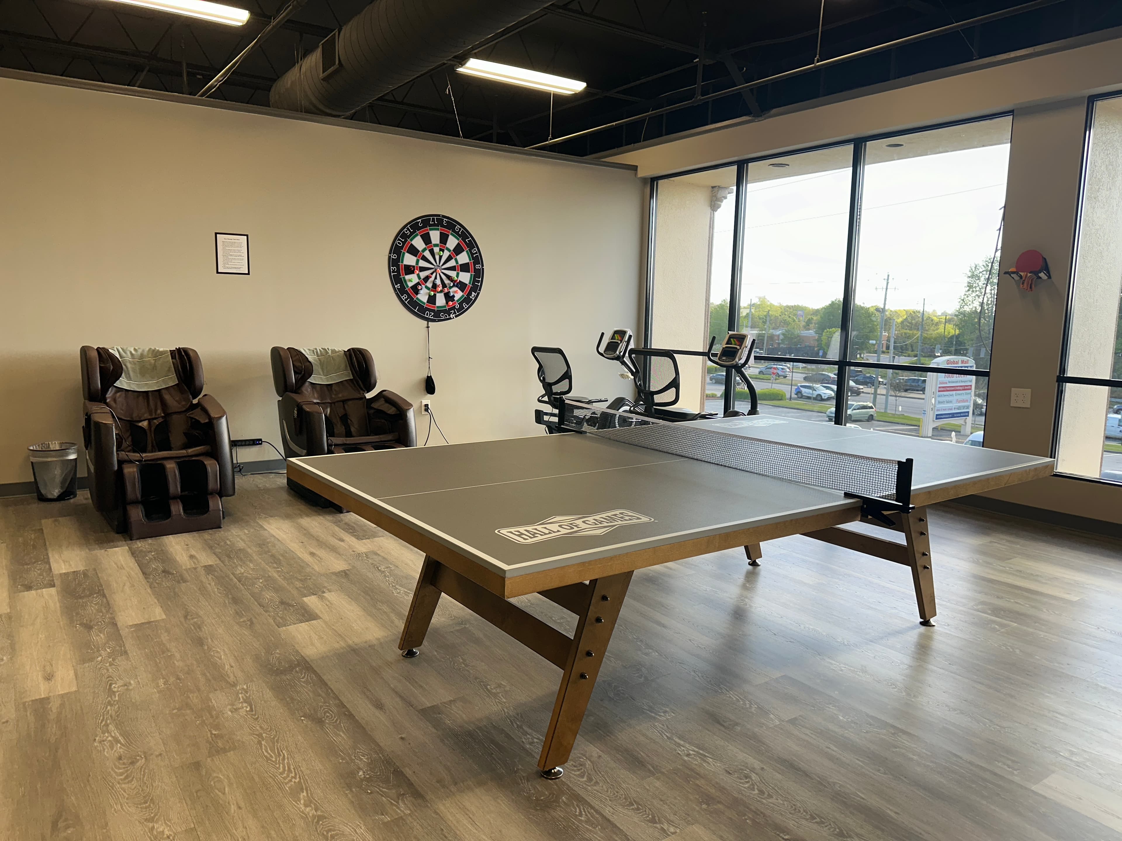 A ping pong table with a dartboard on the wall behind it